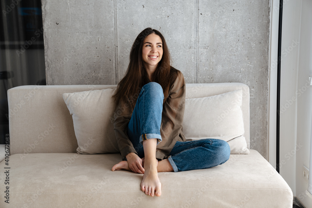 Happy brunette nice girl smiling while sitting on sofa at home Happy brunette nice girl smiling while sitting on sofa at home