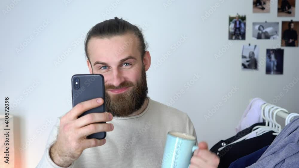 Attractive Young long hair guy is looking in a mirror doing selfie & and drinking coffee Attractive Young long hair guy is looking in a mirror doing selfie & and drinking coffee