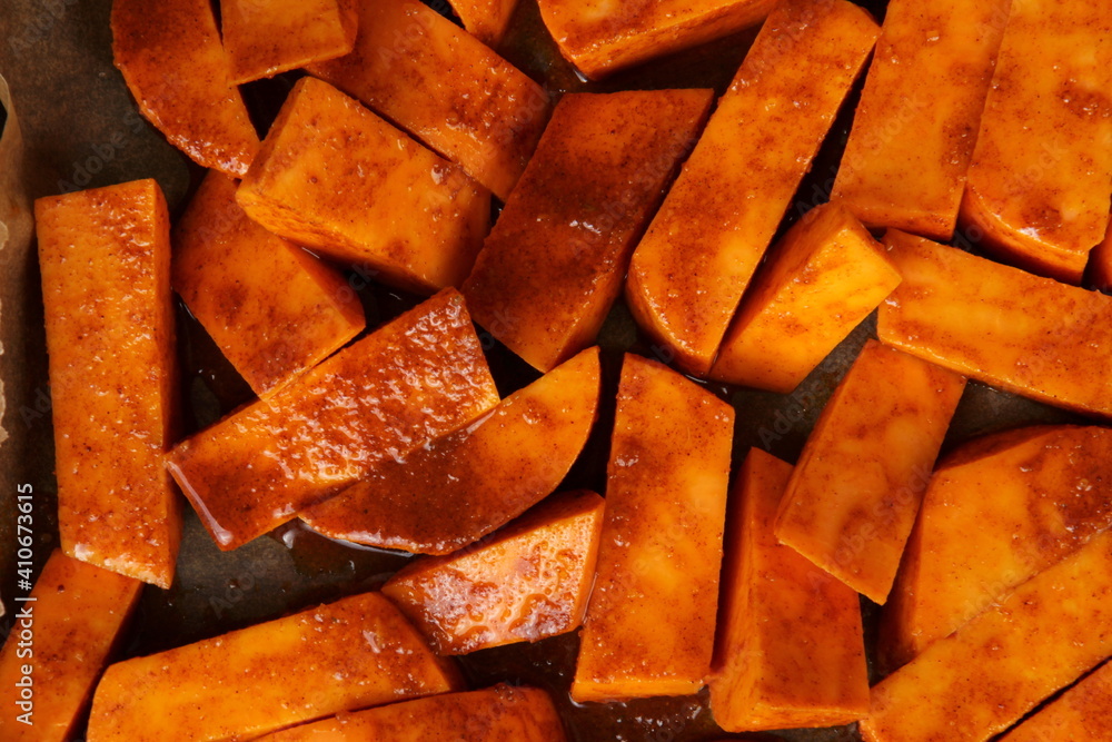 Sliced raw sweet potato with oil and spices on the baking paper, oven pan. Cooking sweet potato or batatas recipe in an oven