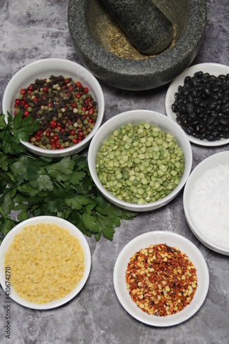 colorful spices and legumes  fresh parsley and stone mortar  pepper  hot pepper  coarse rock salt  black beans and yellow lentils  and colored pepper