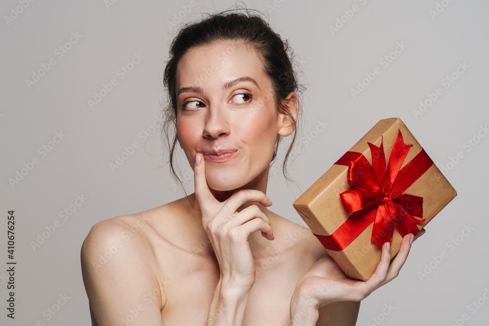 Pleased half-naked woman thinking while showing gift box Pleased half-naked woman thinking while showing gift box