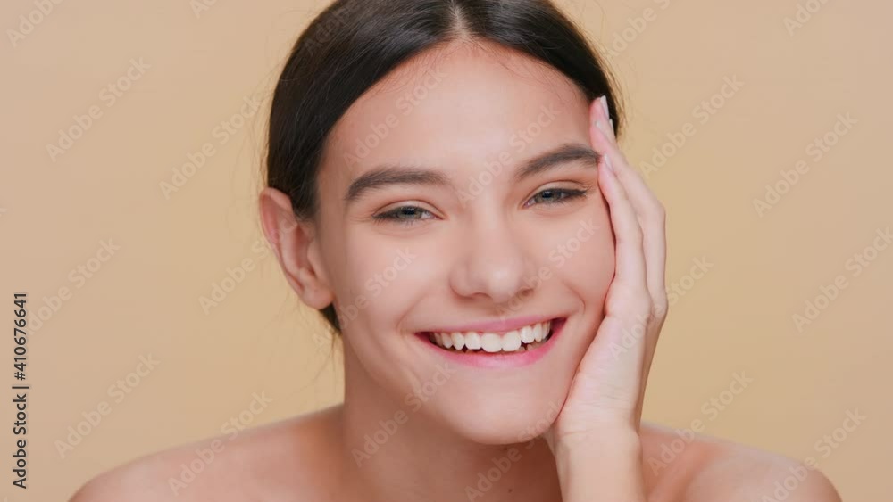 Close-up beauty portrait of young positive dark-haired woman looks at camera, smiles and then laughs putting her hand on her cheek Close-up beauty portrait of young positive dark-haired woman looks at camera, smiles and then laughs putting her hand on her cheek