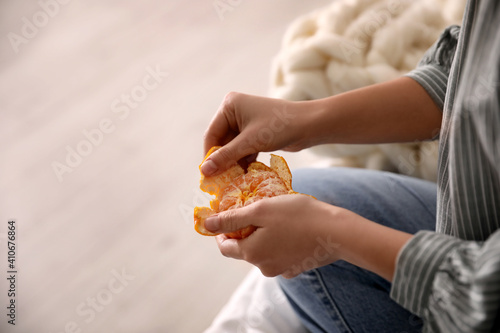 Woman peeling fresh tangerine on blurred background  closeup