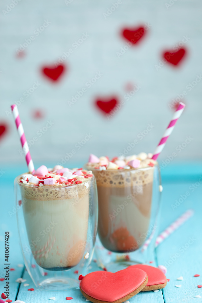 Two glasses of hot coffee or cappuccino with marshmallows and heart-shaped cookies on a blue background. Two glasses of hot coffee or cappuccino with marshmallows and heart-shaped cookies on a blue background.