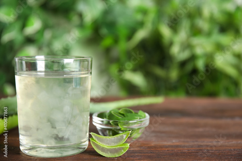 Fresh aloe drink in glass and leaves on wooden table, space for text