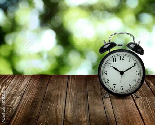 Black alarm clock on wooden table, space for text. Daylight saving time (Spring forward)