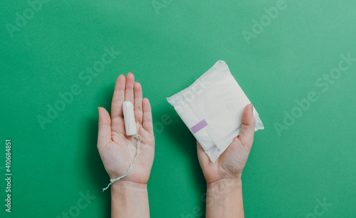 Female hands holding menstrual cup and sanitary pad over green background with copy space