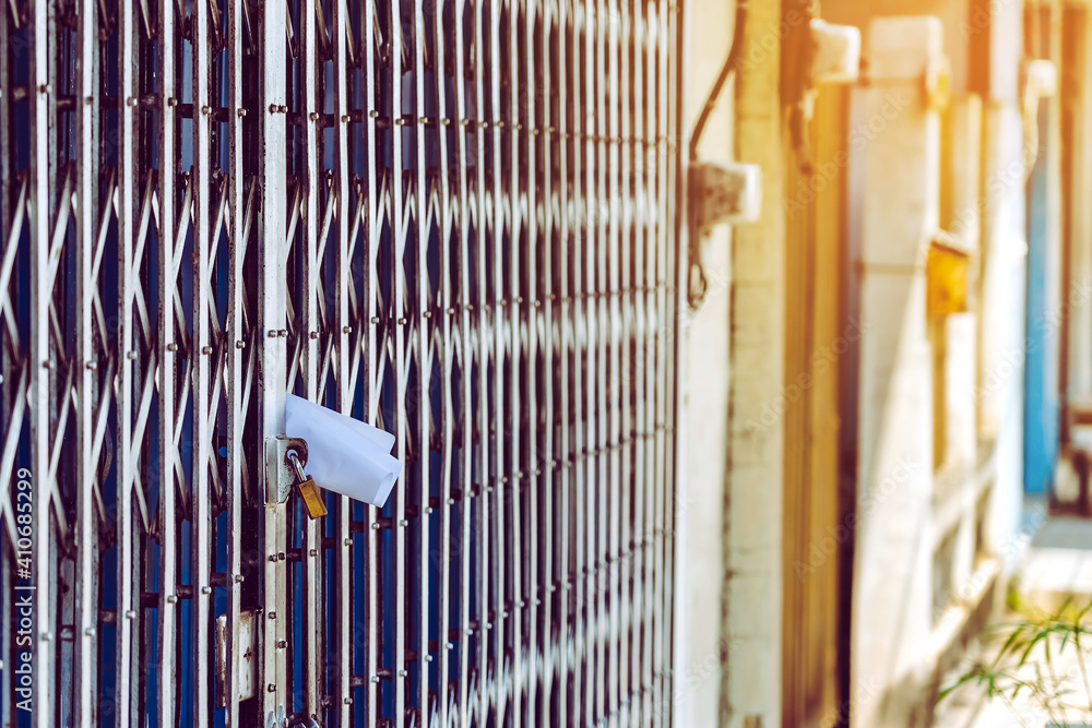 White paper notification attached to closed retractable folding metallic  gate.Metal collapsible sliding grille door normally use at shop houses in  Asia. Bulletin sticking out at the gate of the house. Stock Photo