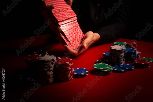 Casino. Poker. The player's hands shuffle the deck of playing cards. Game chips and dice lie on the table against a red background. Game chips for betting in gambling. Dice. Poker chips. 