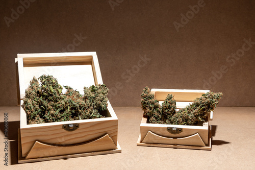 Ready-to-use medical marihuana buds inside two wooden boxes. Selective focus on brown background.