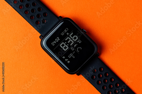 Top view of modern smart watch with fitness tracker on orange background close-up