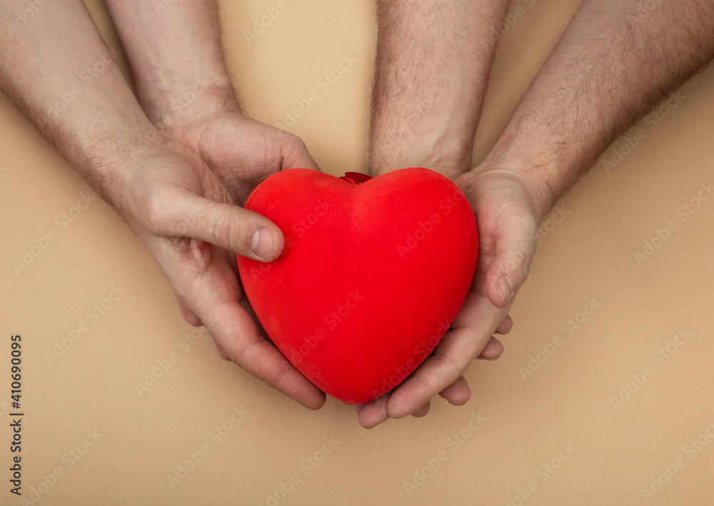 LGBT concept with men hands holding red heart on beige background with copy space. Hands of homosexual couple on set sail champagne color. Same sex love. Gay Valentines card LGBT concept with men hands holding red heart on beige background with copy space. Hands of homosexual couple on set sail champagne color. Same sex love. Gay Valentines card