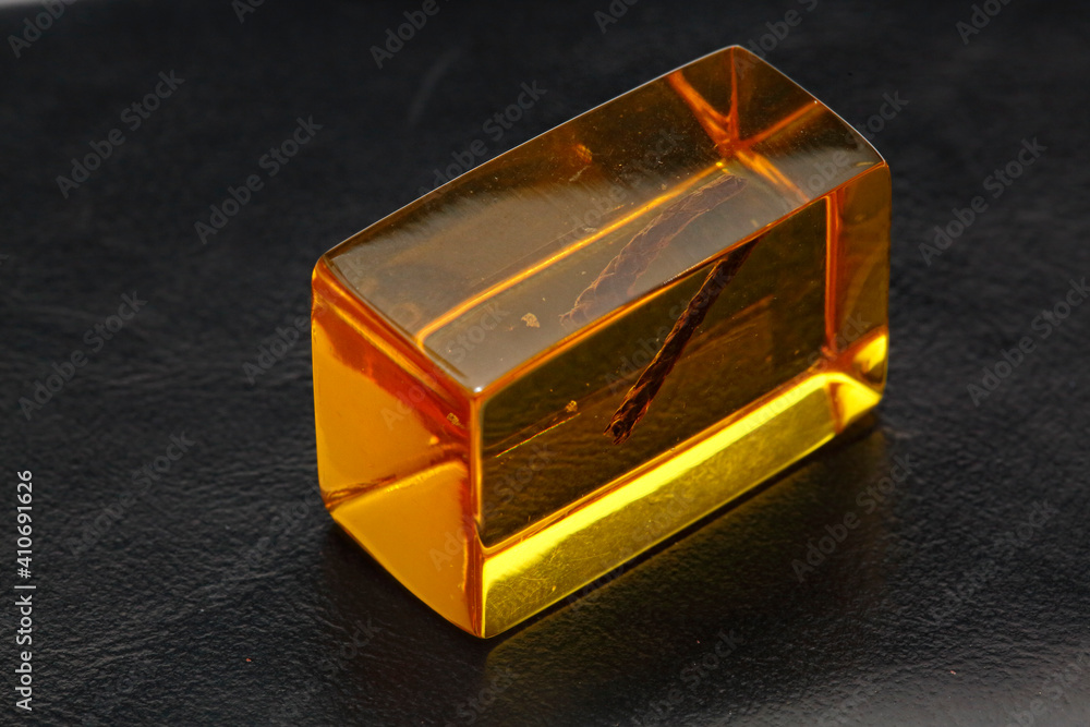 One transparent square piece of amber with patterns on a black background. Sun stone. Semi-precious mineral for jewelry. Fossilized fossil resin. Copal. Patterns and inclusions in amber. Branch One transparent square piece of amber with patterns on a black background. Sun stone. Semi-precious mineral for jewelry. Fossilized fossil resin. Copal. Patterns and inclusions in amber. Branch