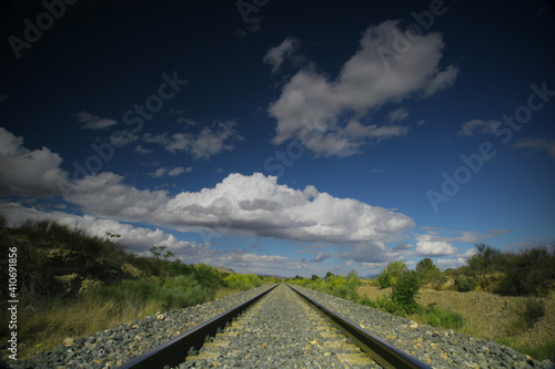 Vía de ferrocarril en recta, y cielo con nubes.