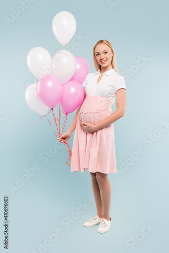 full length of pregnant woman holding balloons on blue