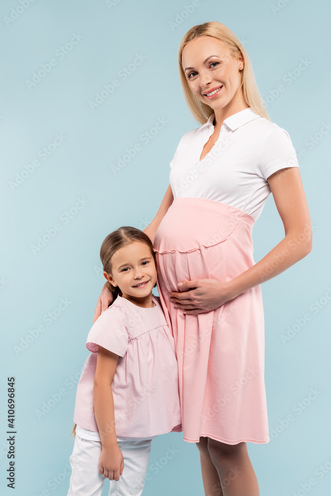 cheerful daughter standing with pregnant mother isolated on blue cheerful daughter standing with pregnant mother isolated on blue