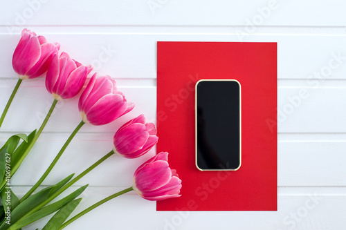 spring pink tulips, smartphone and red sheet of paper on a white background, top view, postcard