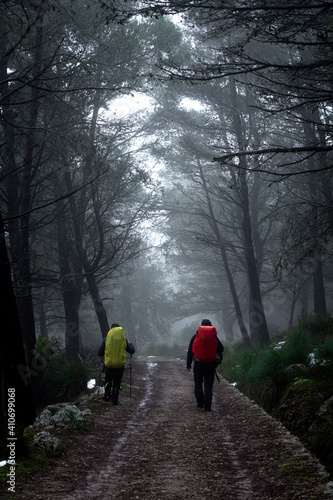 couple of mountaineers walking on a path with fog, dark landscape with traces of snow © MinekPSC