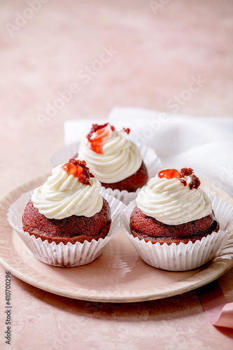Homemade Red velvet cupcakes with whipped cream on pink ceramic plate, white napkin with ribbon over pink texture background.