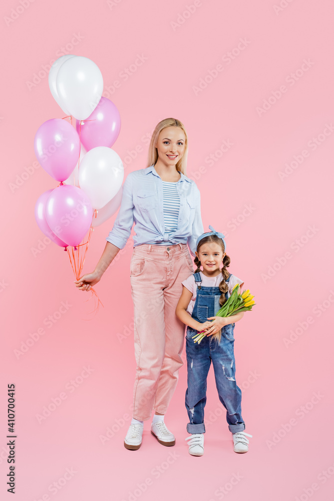 Φωτογραφία full length of kid holding tulips and standing near mother with balloons on pink