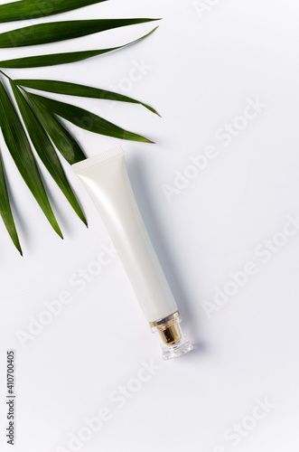 One white tube for cream lies on a white background with a palm leaf