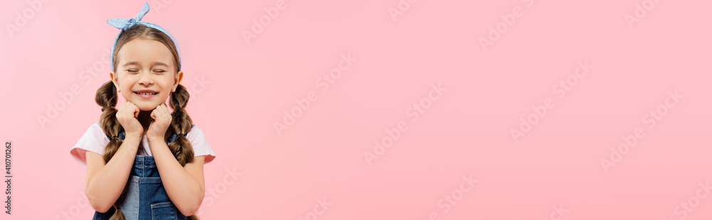 pleased kid with closed eyes smiling isolated on pink, banner pleased kid with closed eyes smiling isolated on pink, banner