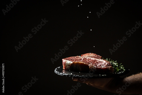 Raw Red Grass Fed T Bone Steak or porterhouse steak of beef Ready to Cook. Cook hand sprinkling salt in a freeze motion on black
