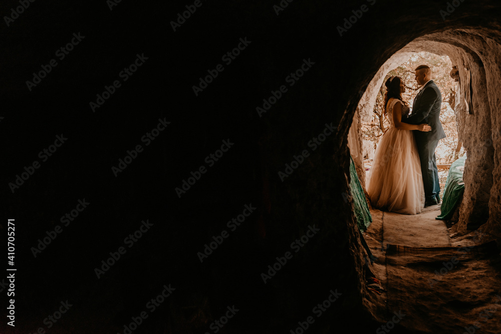 couple bride and groom wedding dress stand in a hole in rock. monastery bakota. natural tunnels rocks of Ukraine