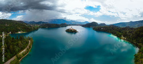 Aerial large wide panoramic view of Lake Bled. Cloudy weather, heavy thunderstorm clouds on the horizon. Summer day. Season of tour and travel. Church of the Mother of God, Slovenia, Europe