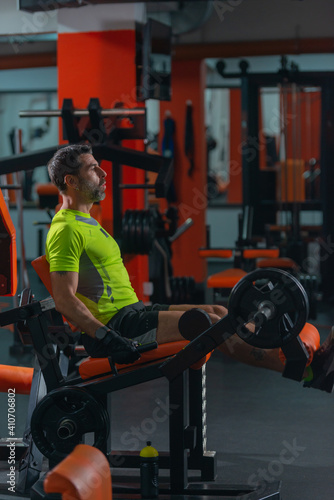 Side view of a middle-aged man with a yellow fluorescent shirt exercising on the machine for legs.