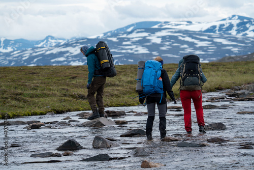 Hiking Friends Manage to wade across the river with helping hand and team work during long Hike in Padjelanta National Park, northern Europe.