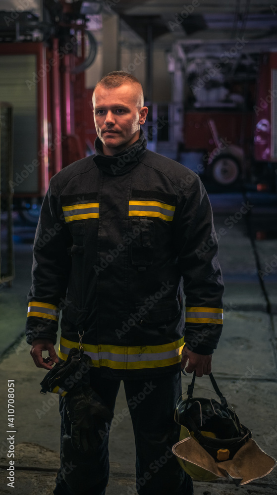 Portrait of young fireman standing inside the fire station. Portrait of young fireman standing inside the fire station.