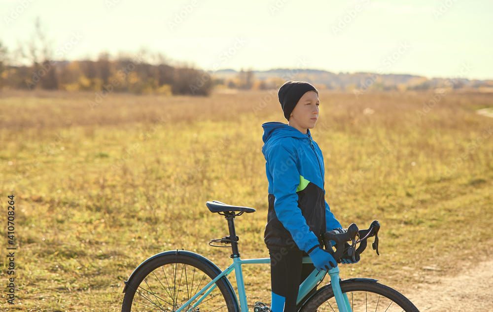 A young cyclist in a tracksuit stopped in a field on a country road