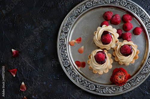 Top view of cupcakes with cream and frozen raspberries. Dark background, iron tray. Selective focus, place for texts