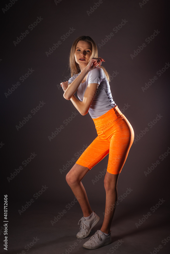 Pretty sports girl with short orange leggings posing isolated on dark background in studio