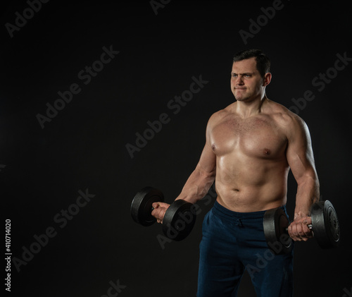 Man strains muscles with dumbbells pumps bicep bare torso Young male business businessman man  portrait strong content  fashion single background black bodybuilder