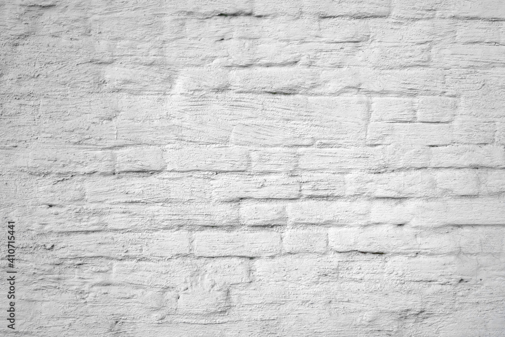 Background of the old cracked brick wall smeared with a thick layer of white paint and plaster. Close-up. Background of the old cracked brick wall smeared with a thick layer of white paint and plaster. Close-up.