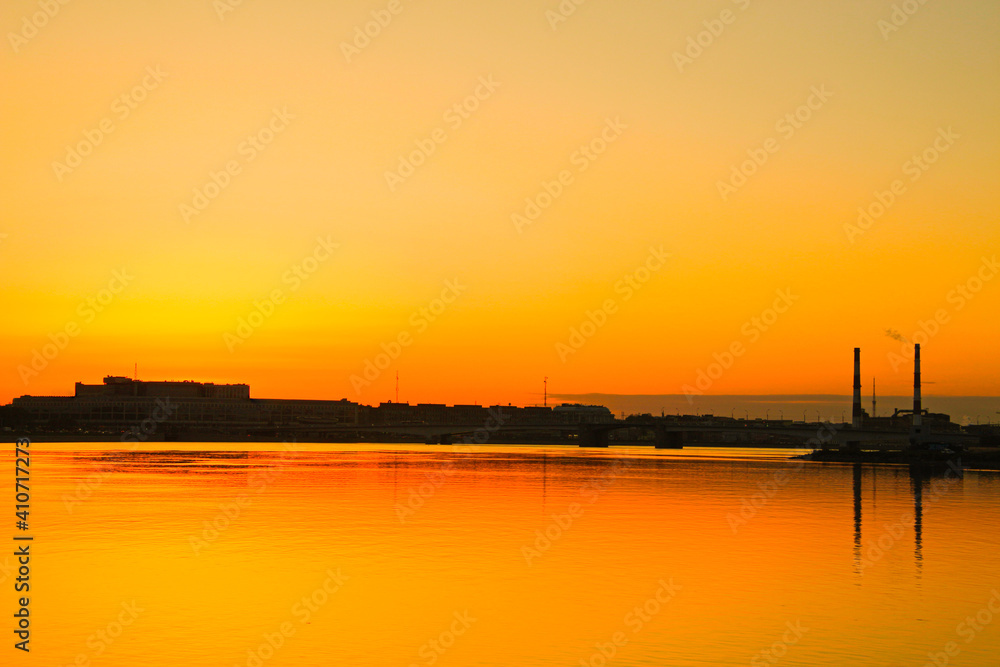 silhouettes of industrial buildings and factory pipes on the shore, reflected in the water at sunset