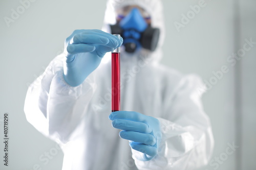 A man in protective suit holds a test tube in his hands. The concept of open vaccines against coronavirus