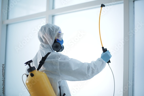 Man in a protective suit with a disinfection cylinder in office