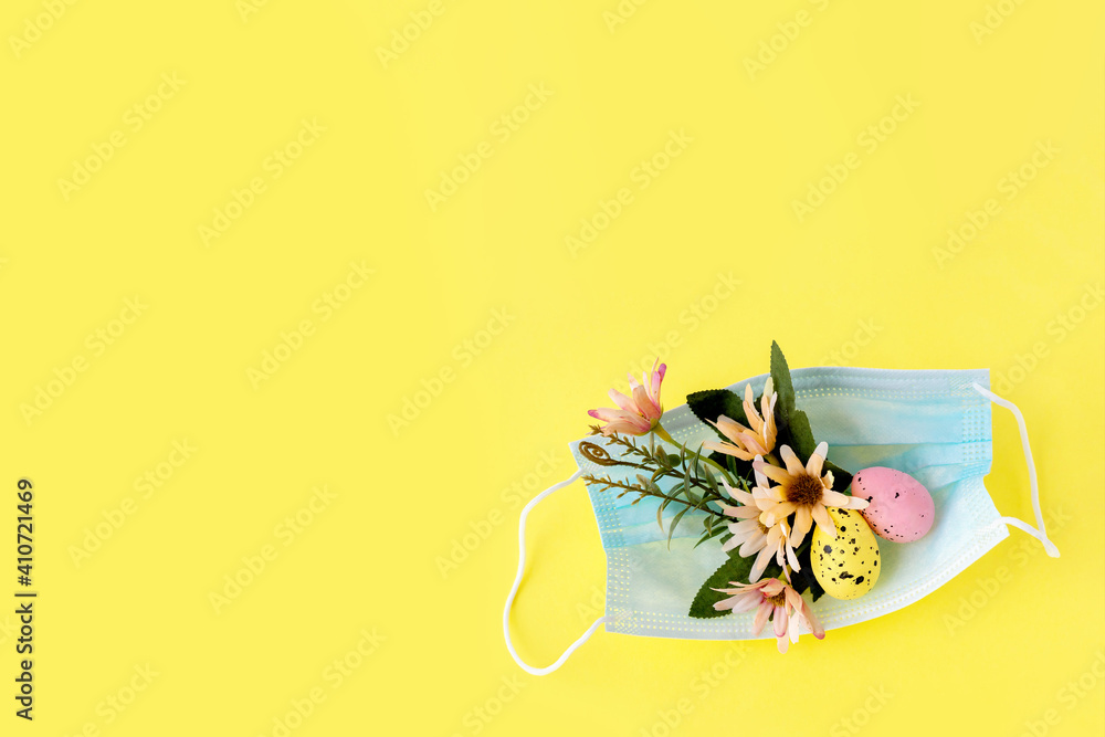 Medical protective face mask and colorful easter eggs isolated on yellow background. Concept of Easter holiday during the global pandemic coronavirus. Flat lay, top view, copy space.