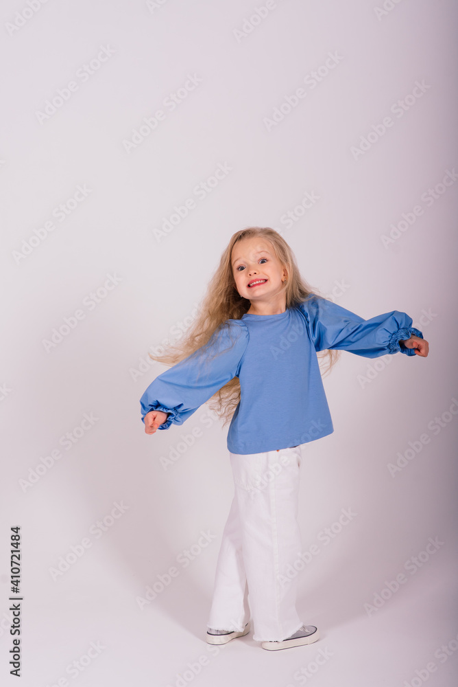 Little blonde girl, she laughing, sitting on floor, posing isolated on blue. Childhood, fashion. Little blonde girl, she laughing, sitting on floor, posing isolated on blue. Childhood, fashion.