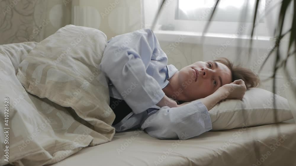 a young Caucasian brown-haired woman in a bed dressed in pajamas wakes up stretches and leaves the bed. Girl waking up from sleep in the morning in pajamas a young Caucasian brown-haired woman in a bed dressed in pajamas wakes up stretches and leaves the bed. Girl waking up from sleep in the morning in pajamas