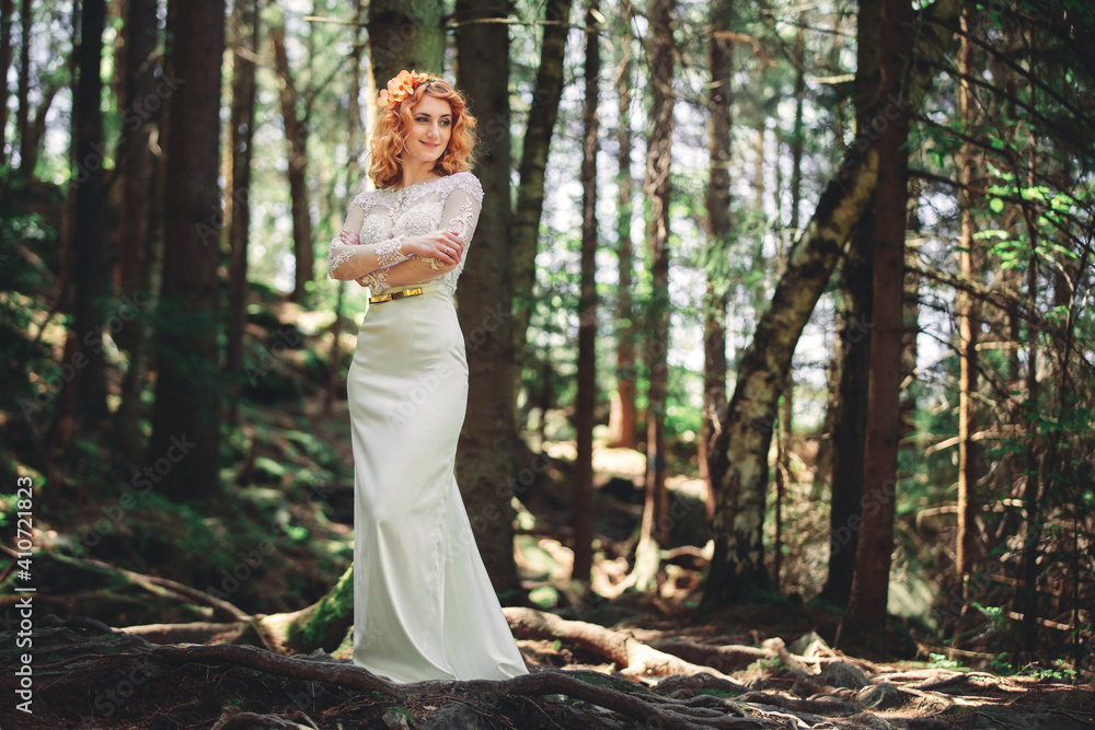 beautiful young red-haired bride in the forest with a floral wreath on her head. woman in long white dress outdoors on summer day. wedding day beautiful young red-haired bride in the forest with a floral wreath on her head. woman in long white dress outdoors on summer day. wedding day