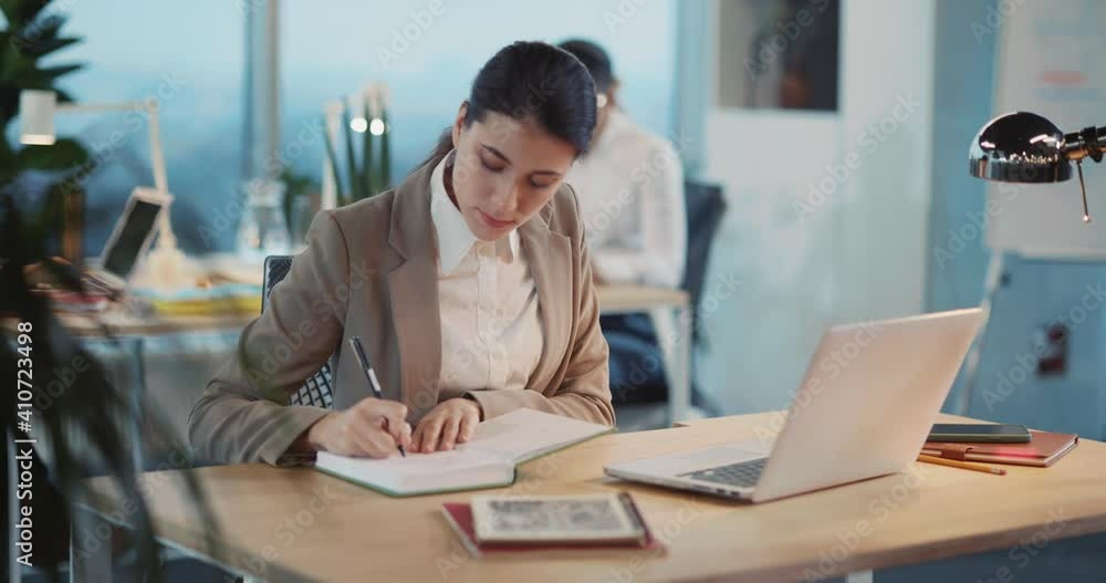 Young Caucasian Woman Sales Assistant Working on Computer Desk Answering Cellphone Call Talking with Client Remotely in Business Office. Young Caucasian Woman Sales Assistant Working on Computer Desk Answering Cellphone Call Talking with Client Remotely in Business Office.