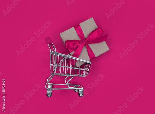 Supermarket trolley and gift box on pink background. Shopping concept.