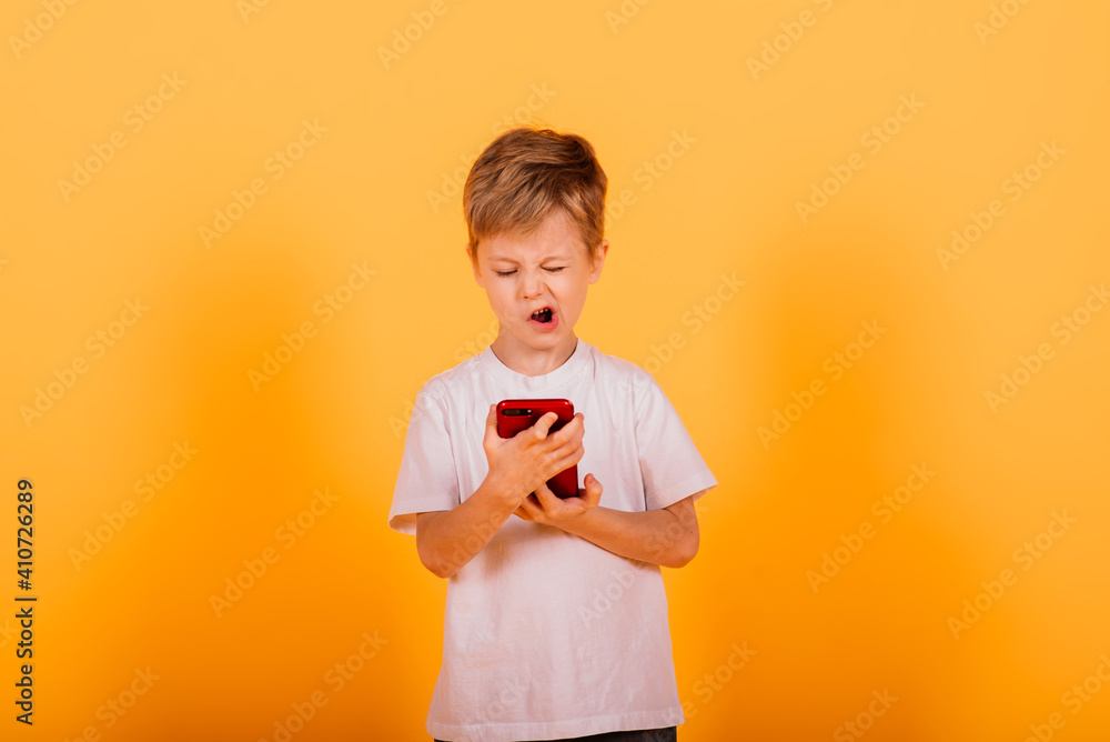 Happy little boy standing and talking on mobile phone over yellow background