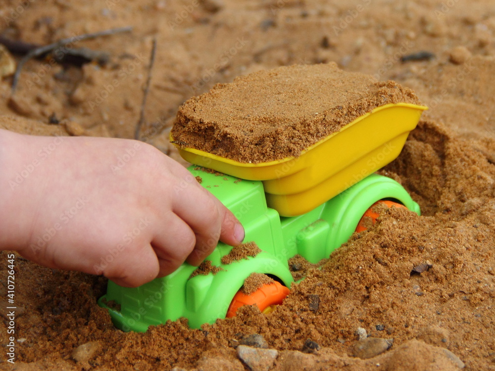 Plastic bright colorful yellow green toy truck loaded tipper sand truck in kid hand close up in outdoor sandbox Plastic bright colorful yellow green toy truck loaded tipper sand truck in kid hand close up in outdoor sandbox