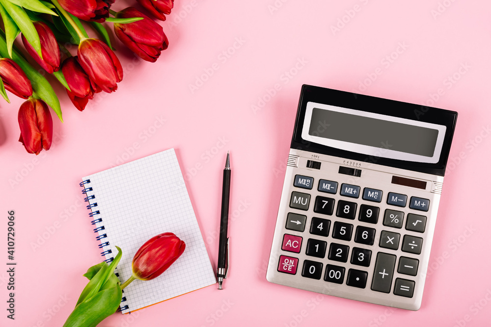 Bouquet of red tulips on pink paper background with calculator, spiral notebook and pen are a template for advertising or visualization of blog with copy space for text. Business holiday. Certificate Bouquet of red tulips on pink paper background with calculator, spiral notebook and pen are a template for advertising or visualization of blog with copy space for text. Business holiday. Certificate