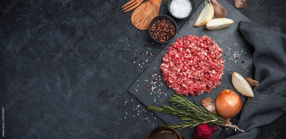Ground turkey meat with pepper, onion and rosemary on a black concrete background. Side view, horizontal, panorama.